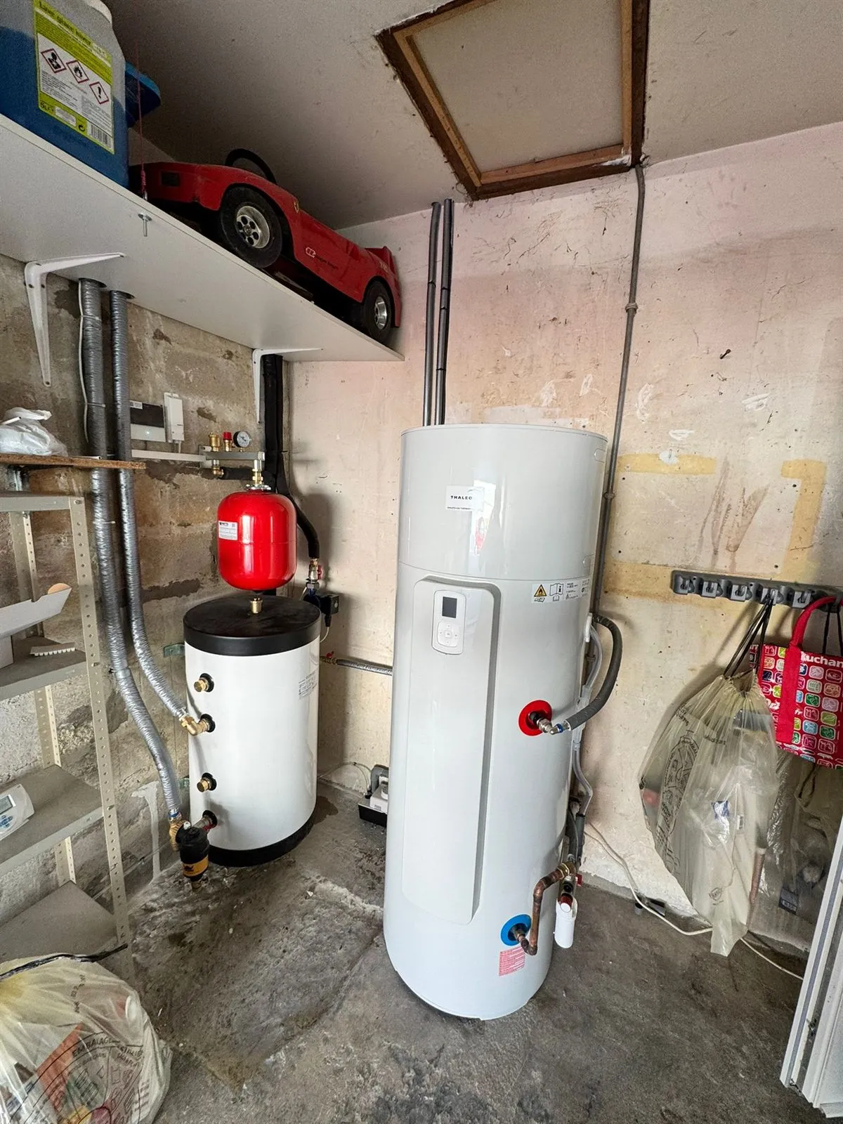 Ballon thermodynamique installé dans un garage, à côté d’un vase d’expansion rouge