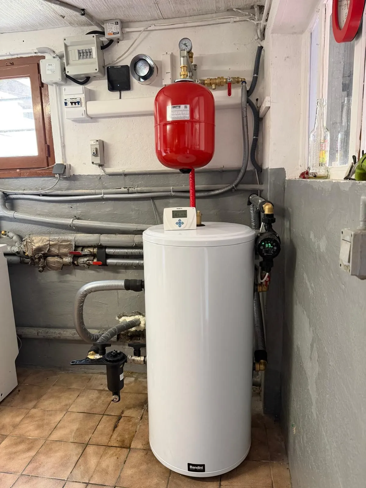 Ballon d’eau chaude installé dans un local technique ancien, sous un vase d’expansion