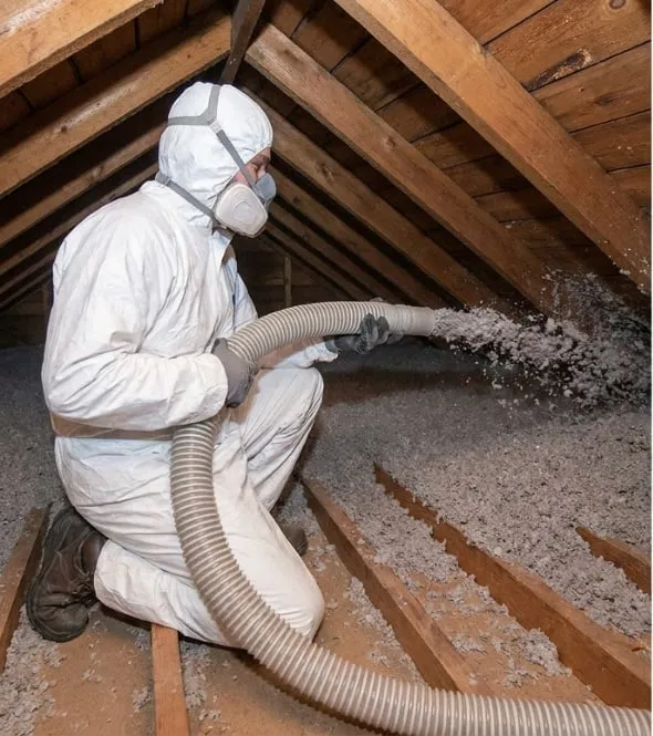 Technicien en combinaison soufflant de l’isolant en flocons entre les solives de combles