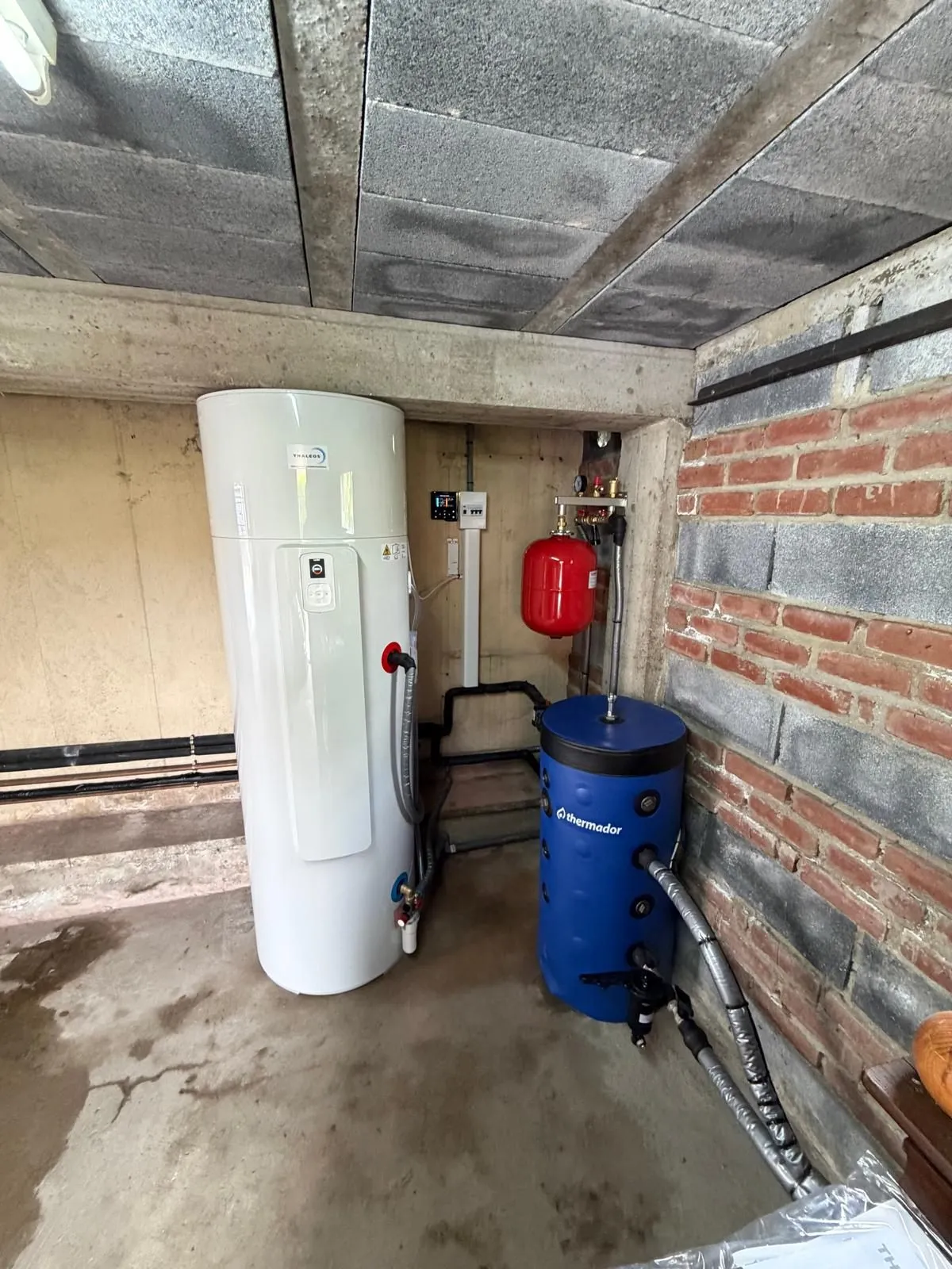 Ballon d’eau chaude blanc et ballon tampon bleu installés dans un garage en parpaings