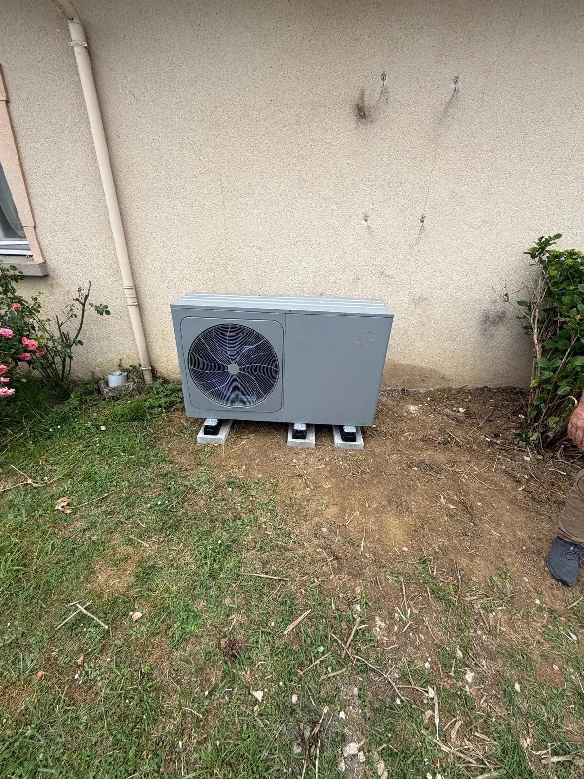 Unité extérieure de pompe à chaleur posée sur plots béton au pied d’une façade claire