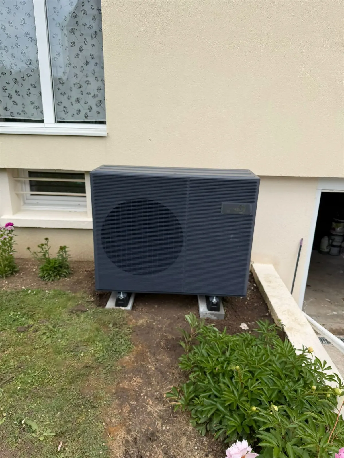 Unité extérieure de pompe à chaleur adossée à une façade, au bord d’un jardin