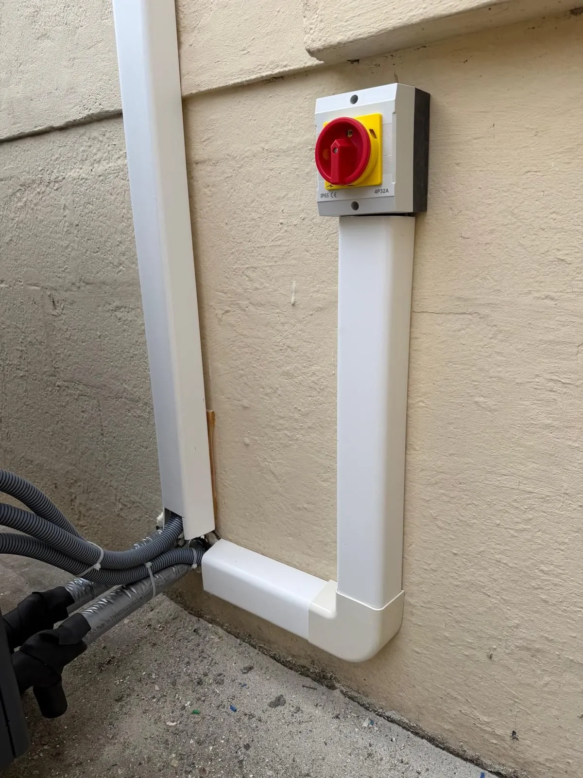 Interrupteur de proximité rouge et goulotte de liaison fixés sur un mur extérieur